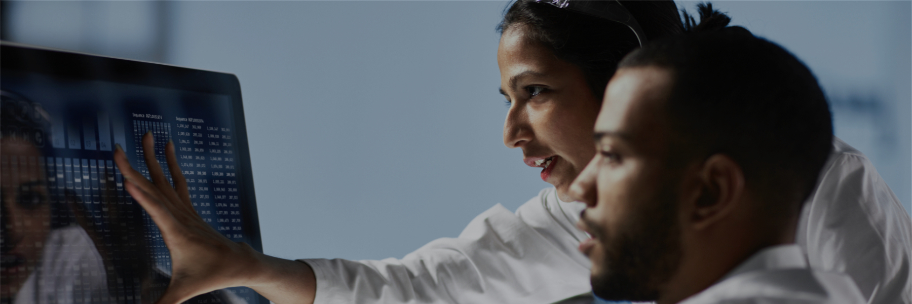 Image of two hospital lab workers reading the screen of a desktop computer